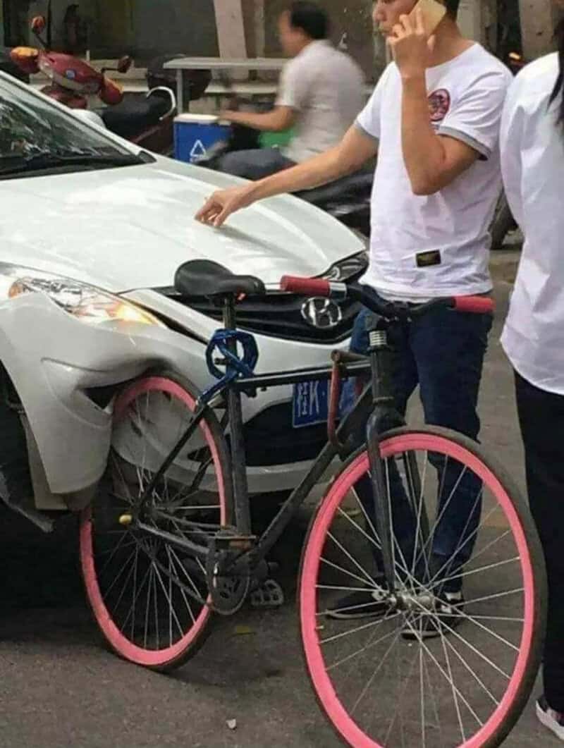 Person touching a white car with a pink and black bicycle in front of it.