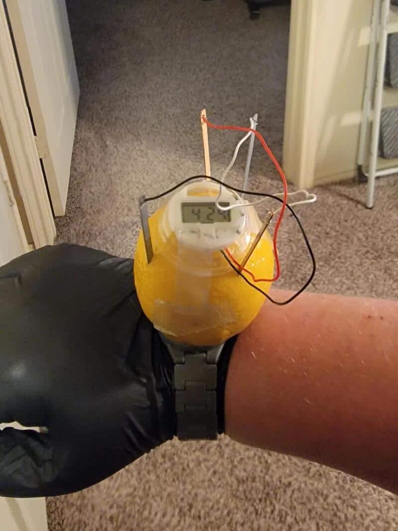 Thermometer attached to a yellow container on a person's wrist, showing 42°C.