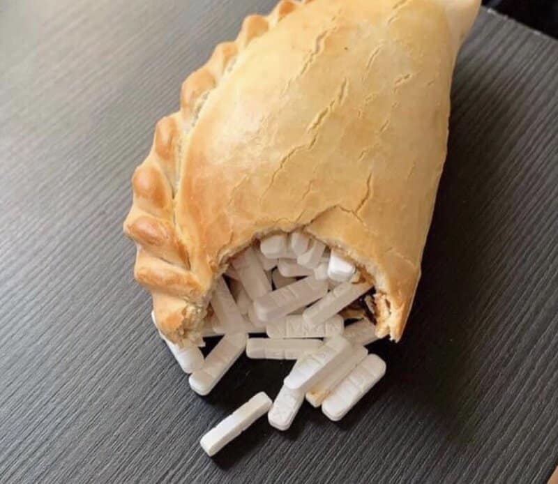 Pie with white pills spilling out of it on a black surface.