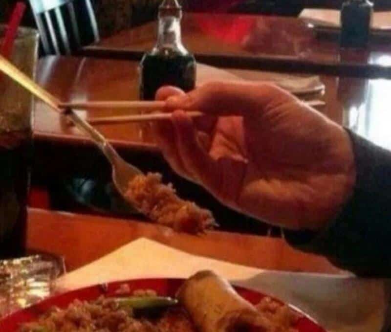 Person holding chopsticks with a piece of food over a plate of Asian cuisine.