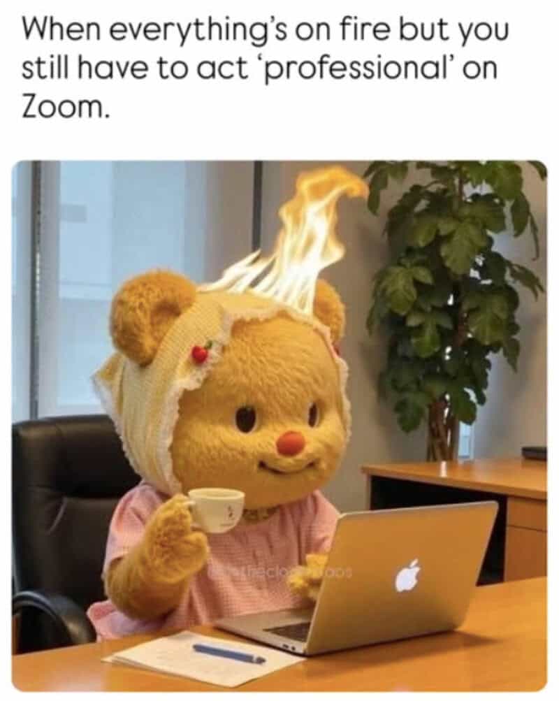 Teddy bear with a fire on its head working on a laptop at a desk.