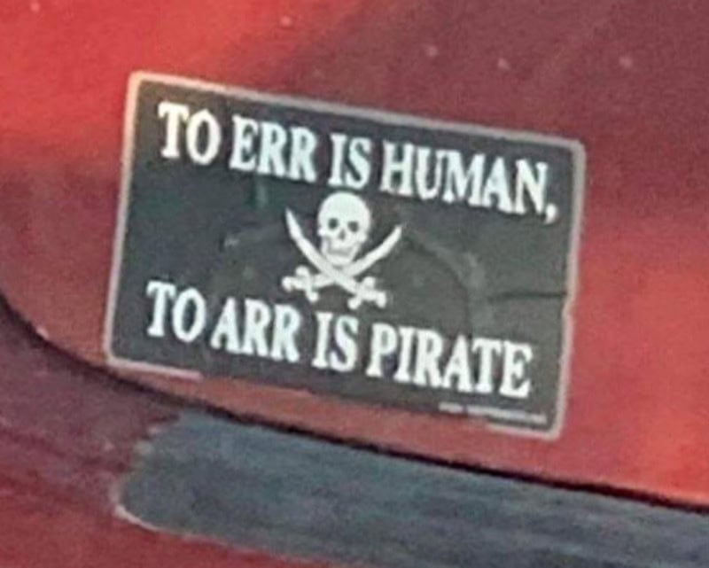 Sign reads 'To Err is Human, To Arr is Pirate' with skull and crossbones.