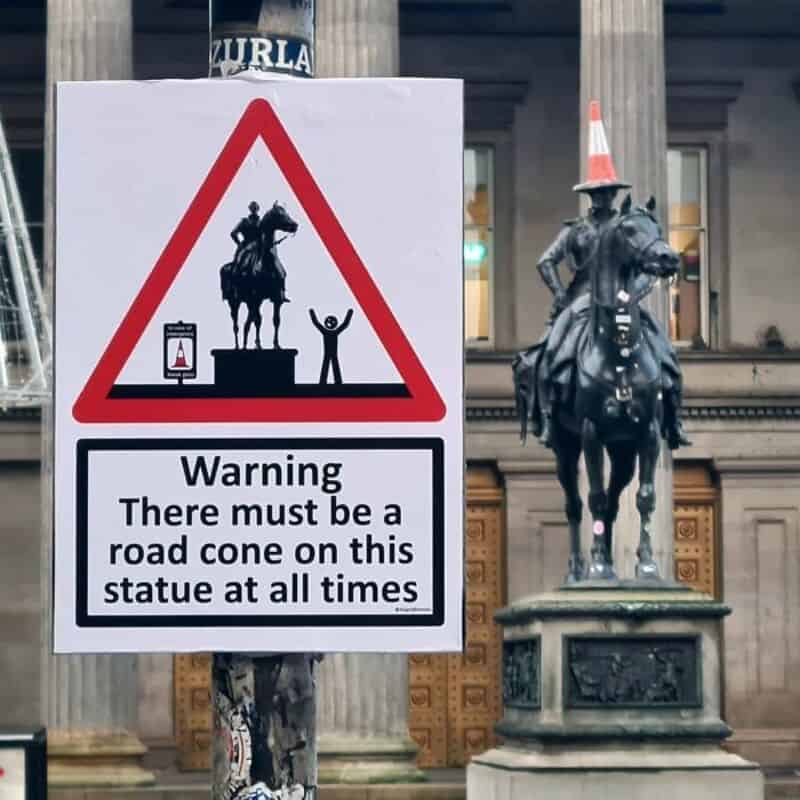 Warning sign about a road cone on the statue at all times.