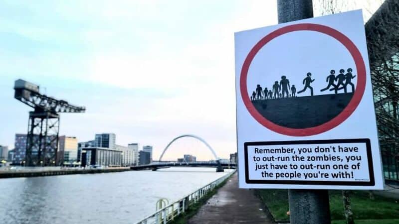 Sign warning about zombies with a humorous message about out-running them.