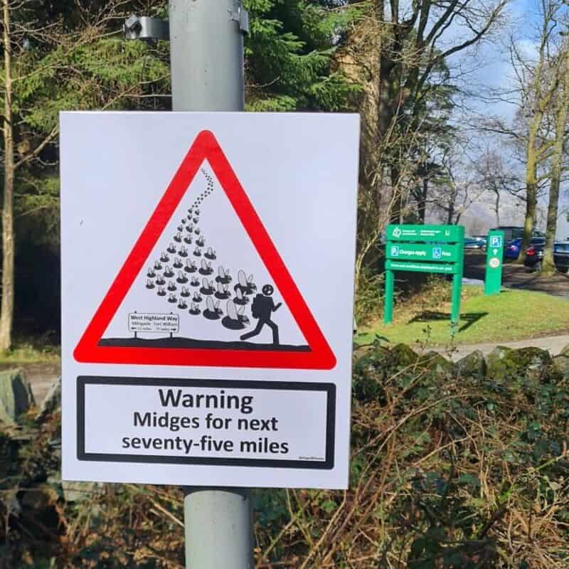 Warning sign for midges for next 75 miles with a cartoon of a person swatting midges.