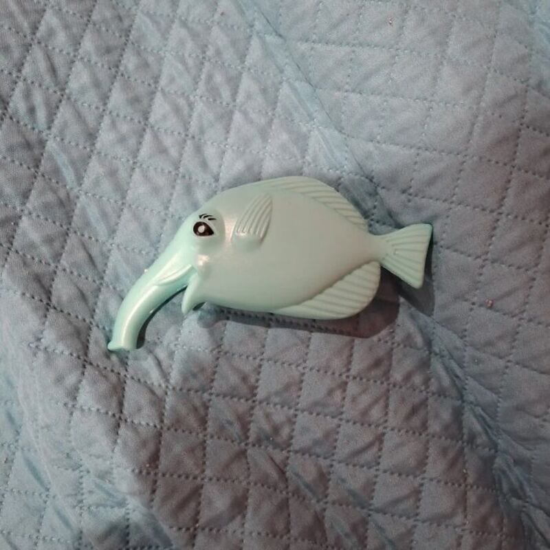Plastic fish-shaped object on quilted fabric background.