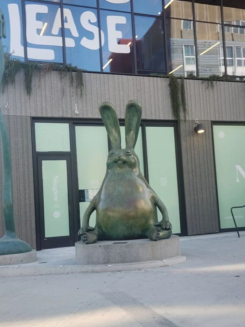 Large rabbit sculpture with long ears sitting outside a building.
