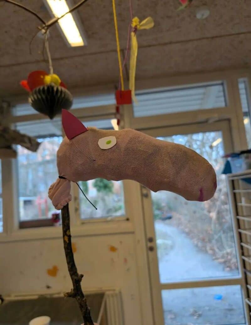 Handmade plush horse with pink ears, white eye, and a branch neck, hanging indoors.