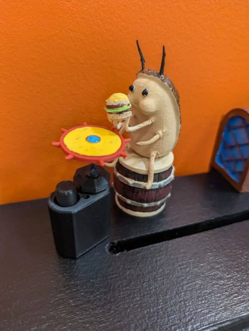 Hedgehog figurine holding a burger and a yellow plate with a blue dot, on a black surface.