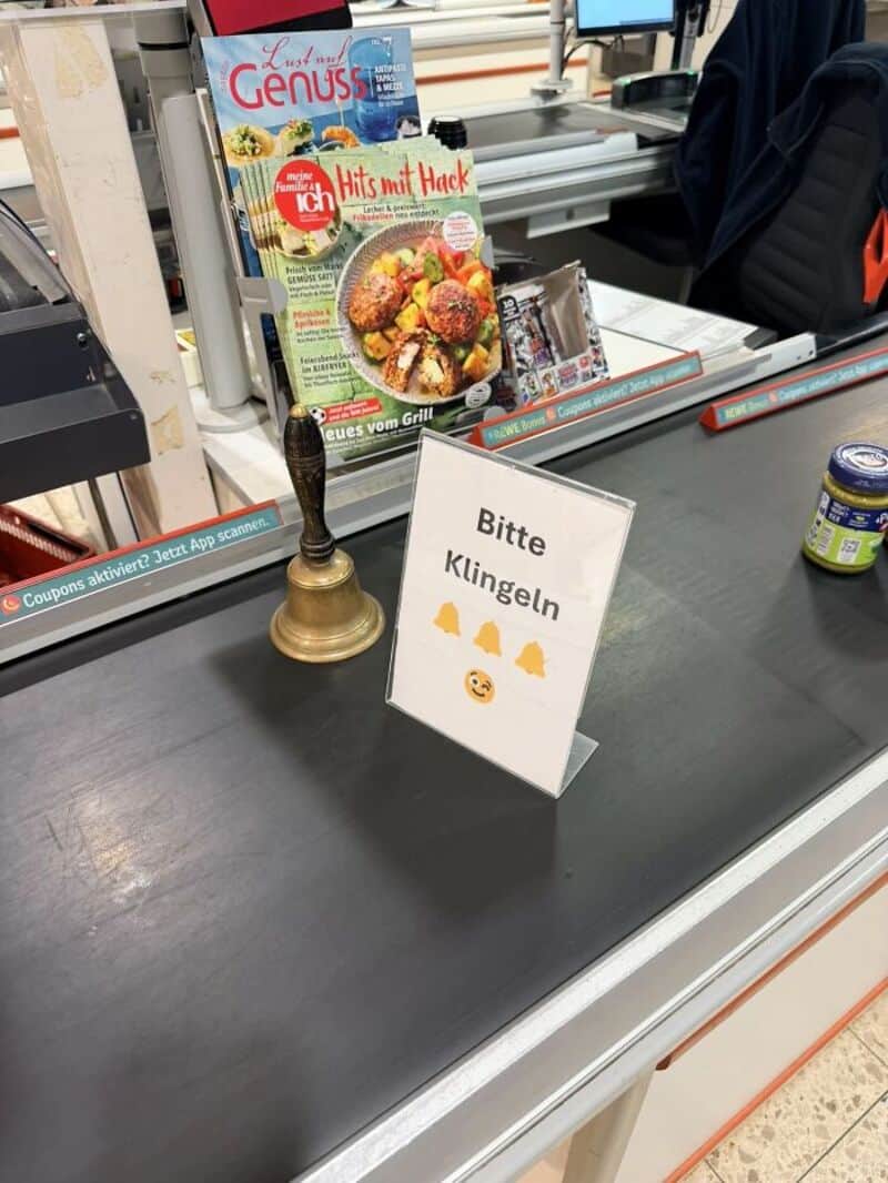 Sign on checkout counter says 'Bitte Klingeln' with a bell icon and smiley face.