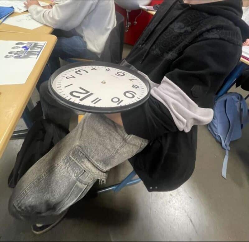 Person holding a large clock with a white face and black numbers.
