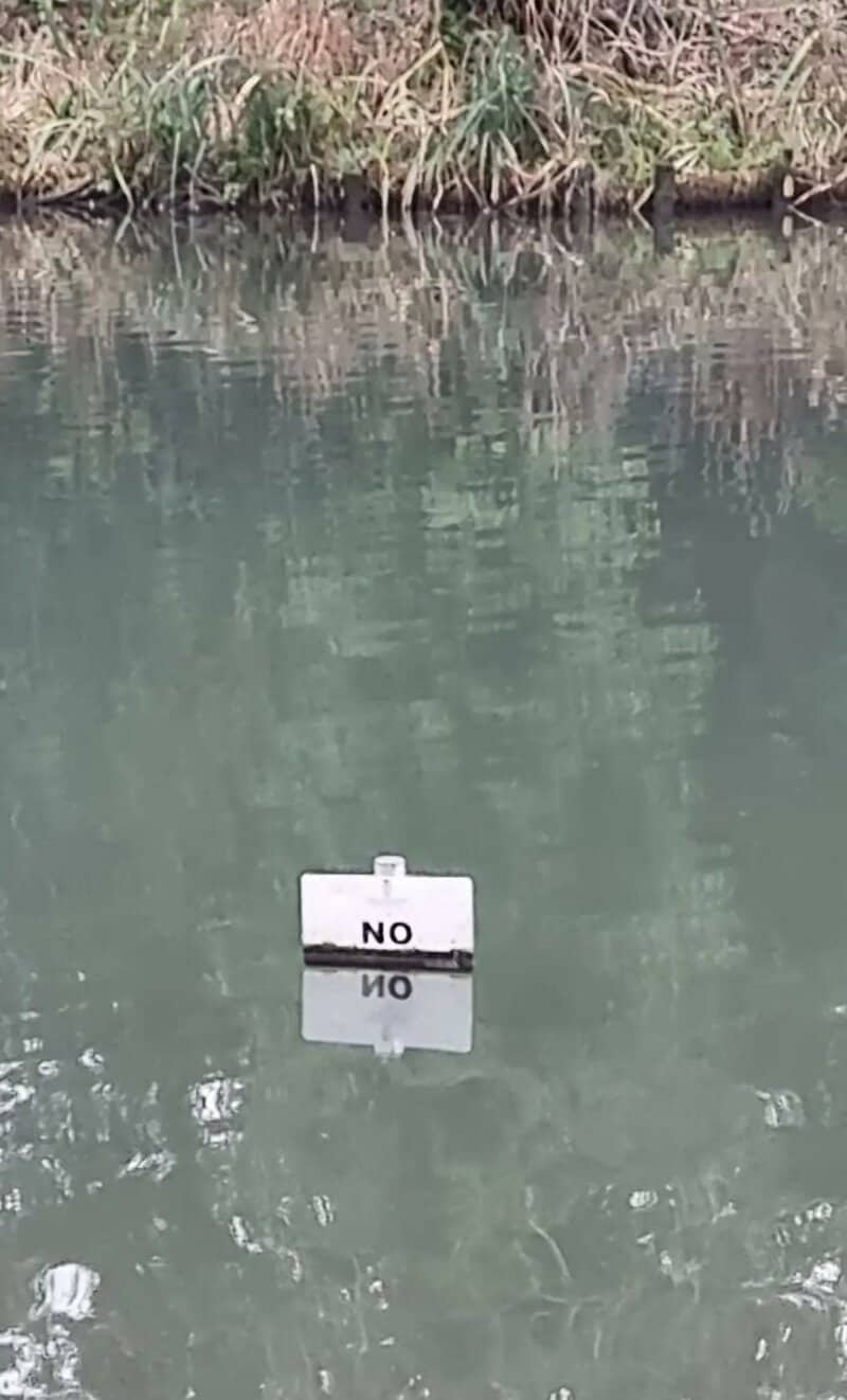 A sign in the water that says 'NO' with a reflection below.
