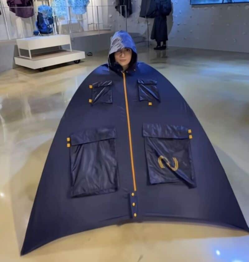 Person in a large, dark blue raincoat with a hood, inside a modern indoor space.