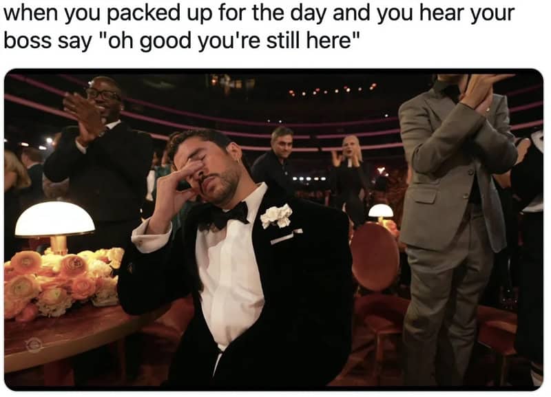 Man in tuxedo at awards show with hand on face, others clapping around him.