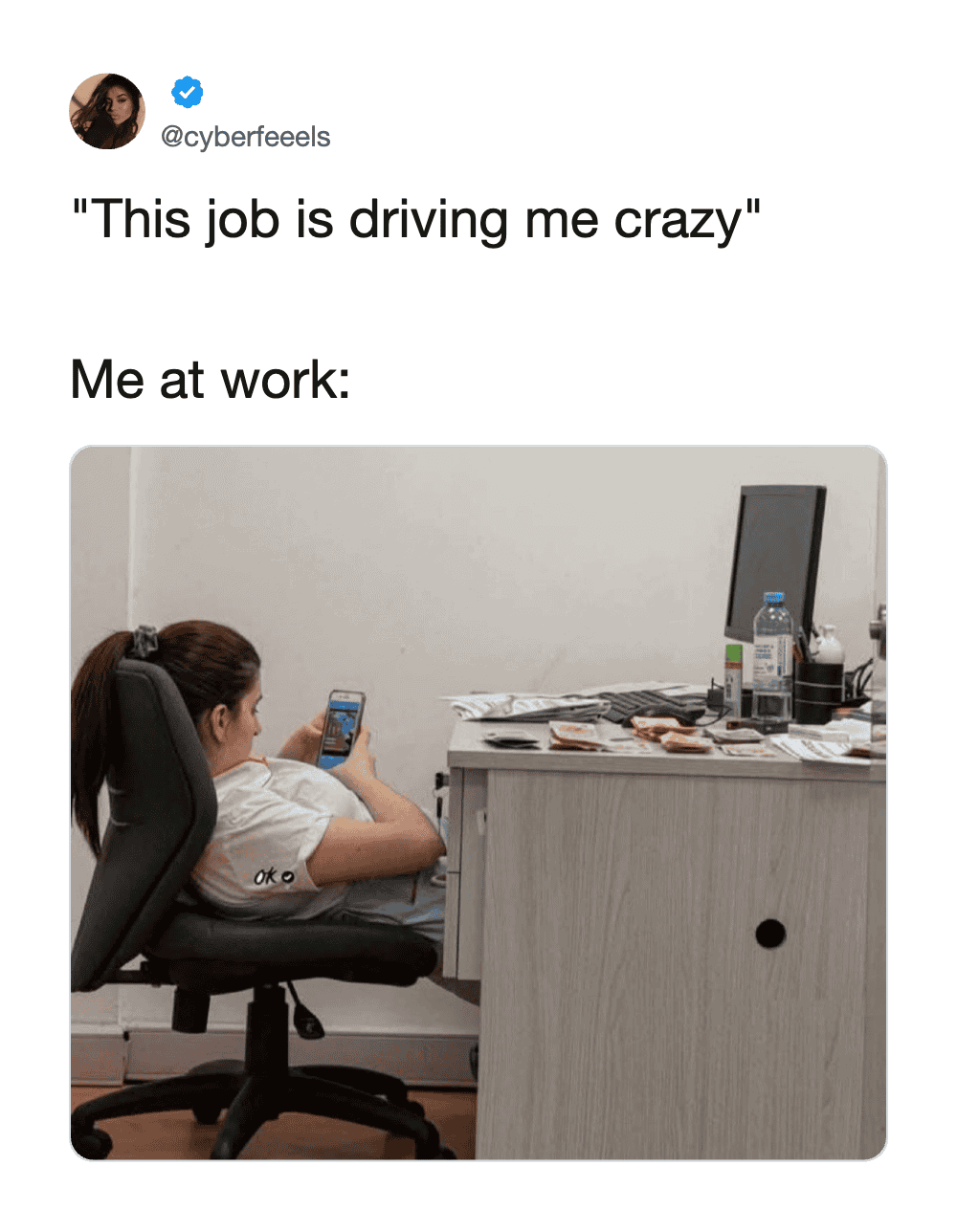 Person at work looking at phone with desk cluttered with items.