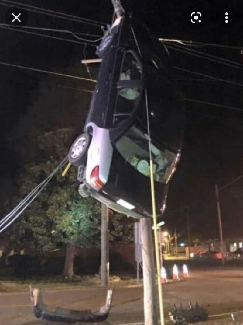 Car hanging from power lines after crashing into utility pole.