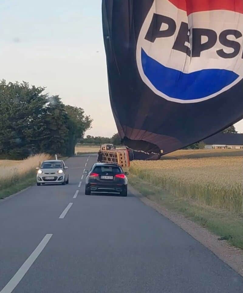 Hot air balloon with Pepsi logo blocking the road, cars driving past.