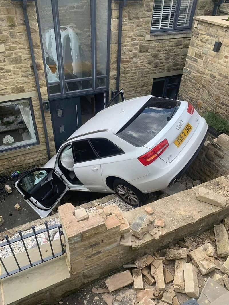 White Audi car crashed into a brick wall, partially hanging over a ledge.