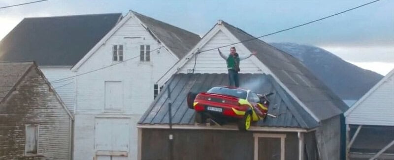 Car parked on roof of a house with a person standing nearby.