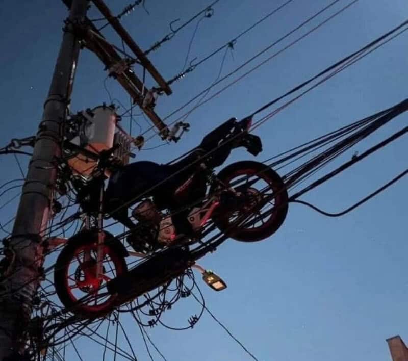 Motorcycle parked on power lines, with wires and pole in the background.