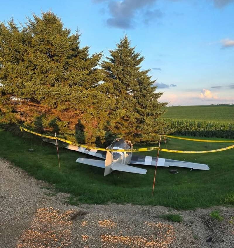 Small airplane crashed into trees, surrounded by caution tape in a rural area.