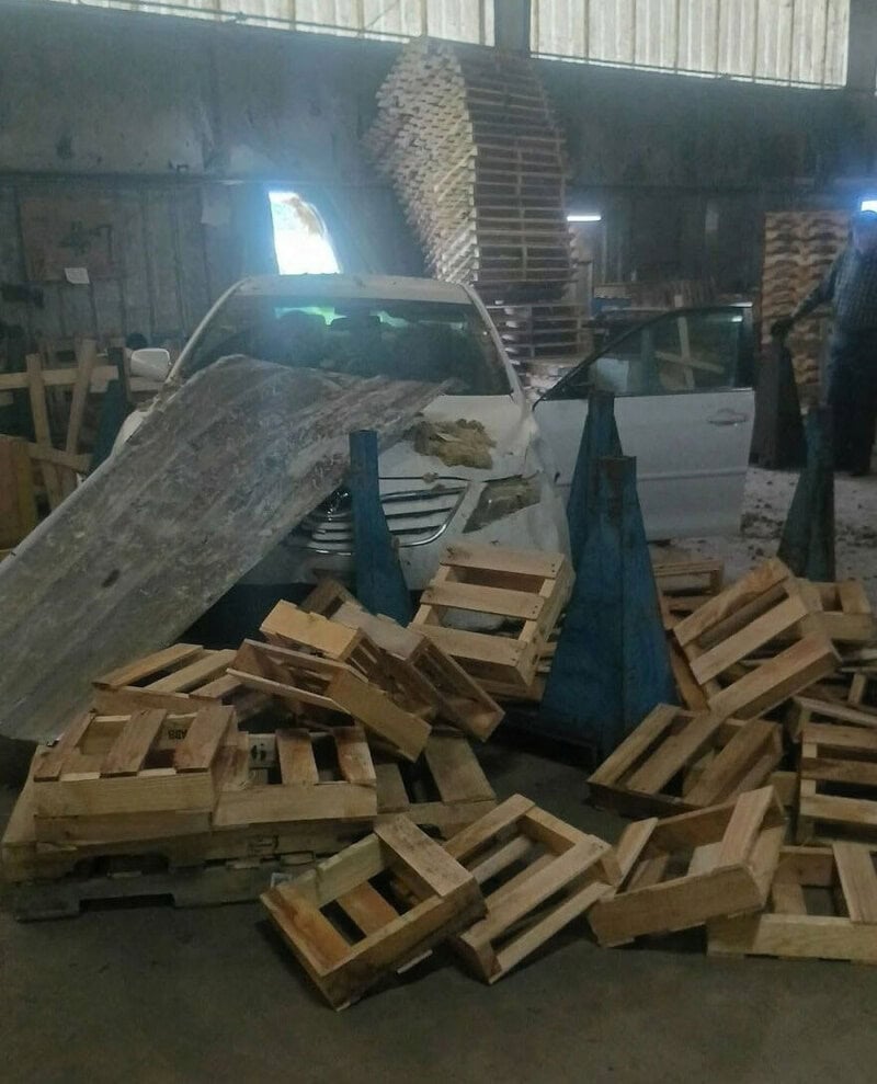 Car crashed into wooden pallets in a warehouse, causing a mess.