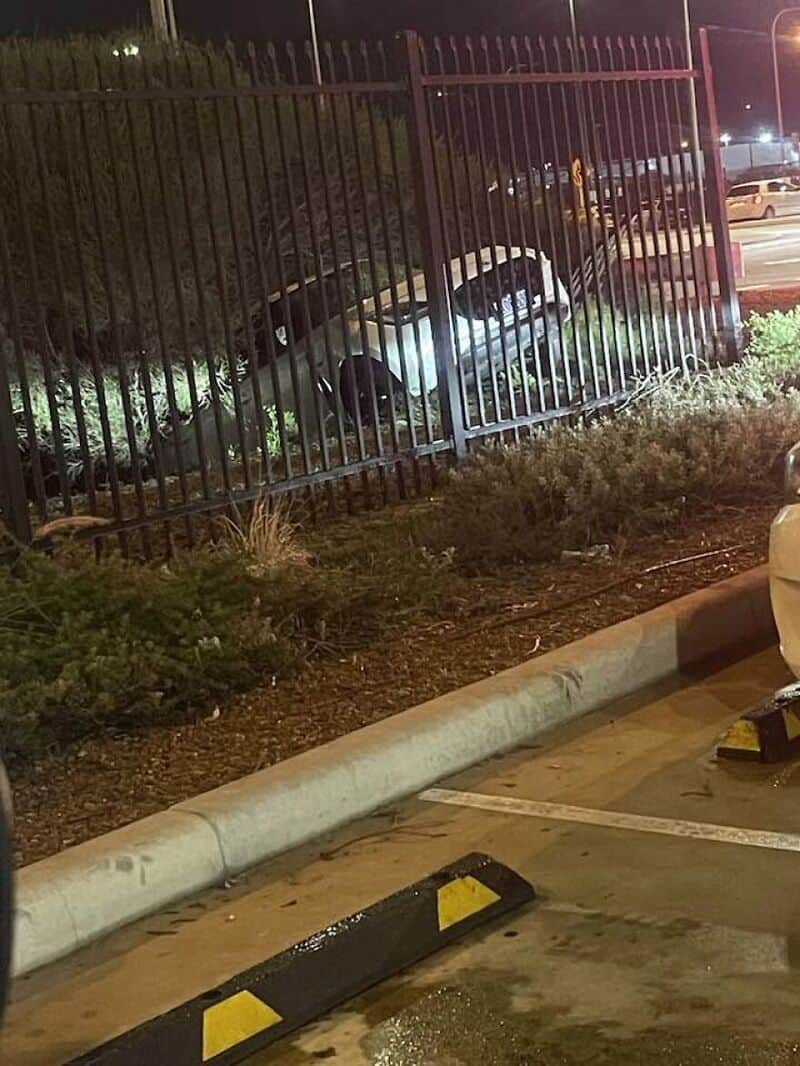 Car crashed into a fence in a parking lot at night.