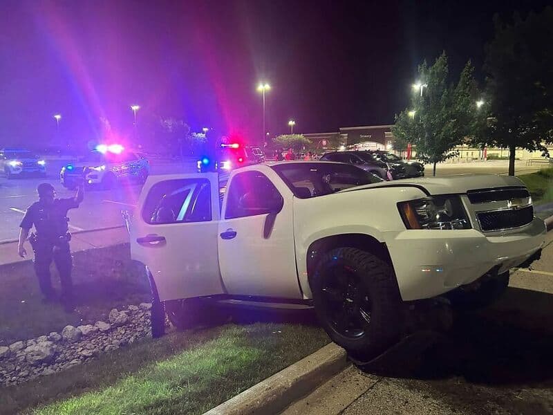 White SUV crashed into parking lot curb with police cars in background.