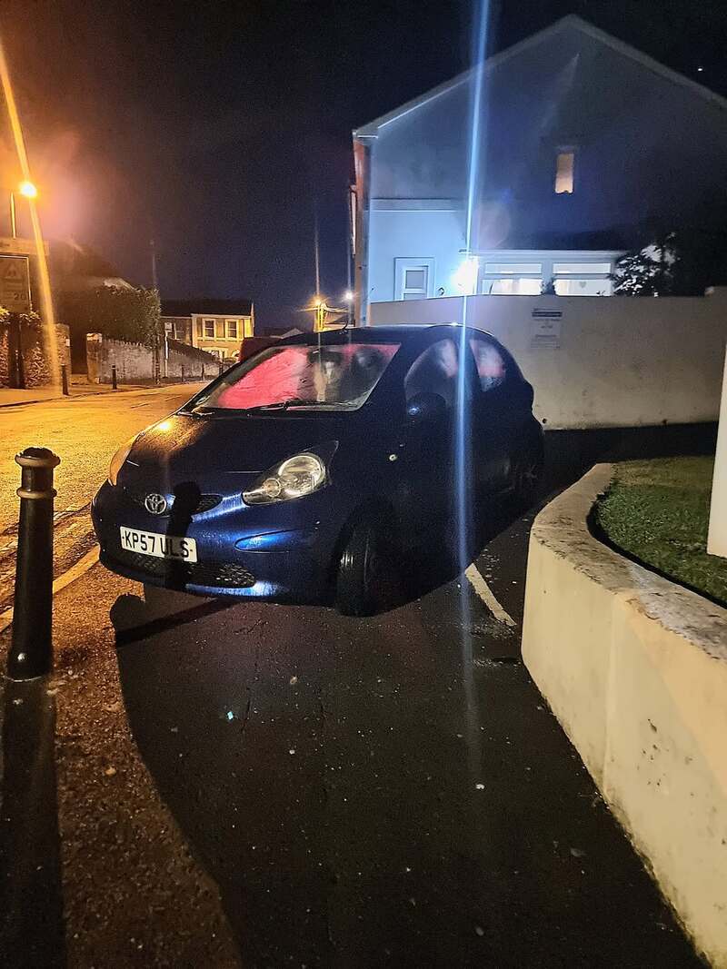 Black car parked on sidewalk next to a white wall at night.