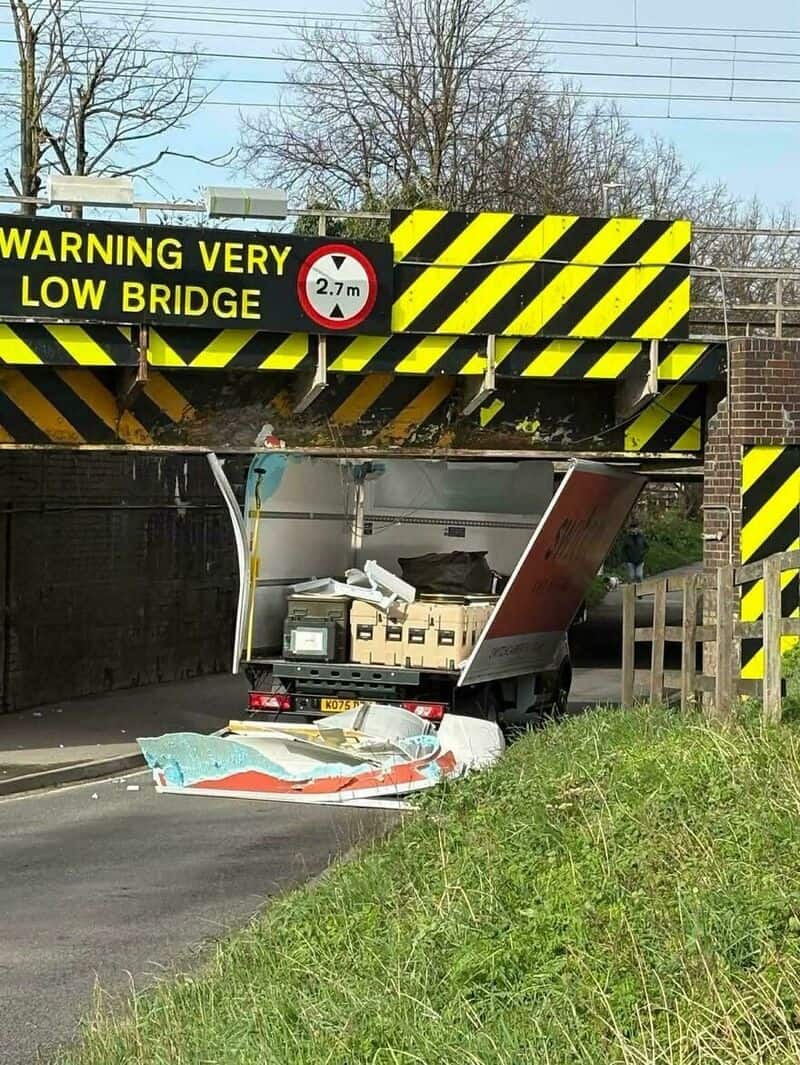 Car crashed into low bridge, debris on road, warning sign visible.