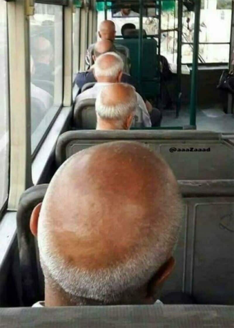 Bald man with white hair on the sides sitting on a bus with other passengers.