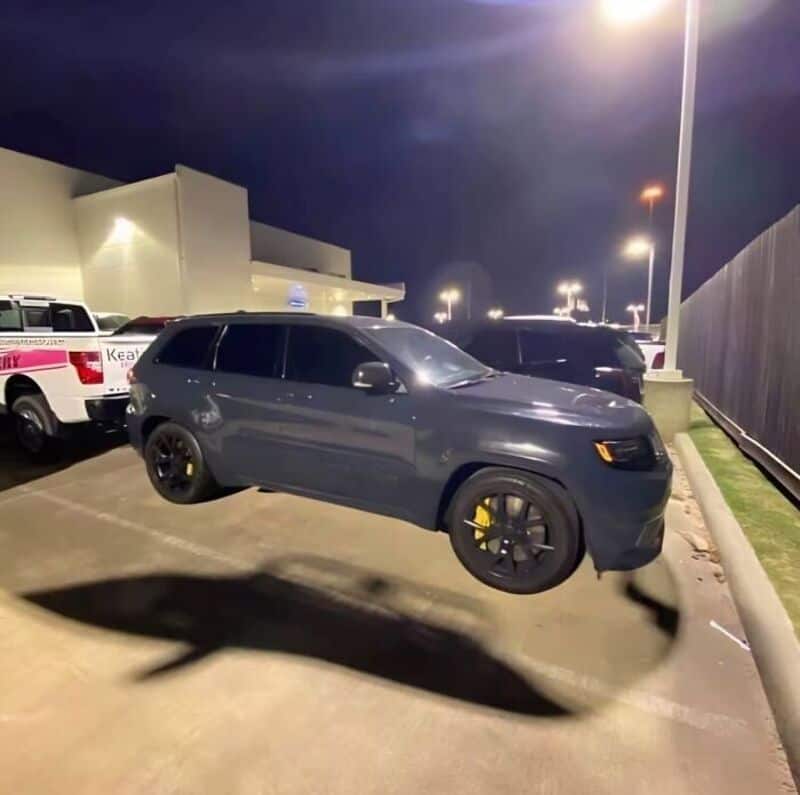 Black SUV with yellow brake calipers casting a shadow in a parking lot at night.