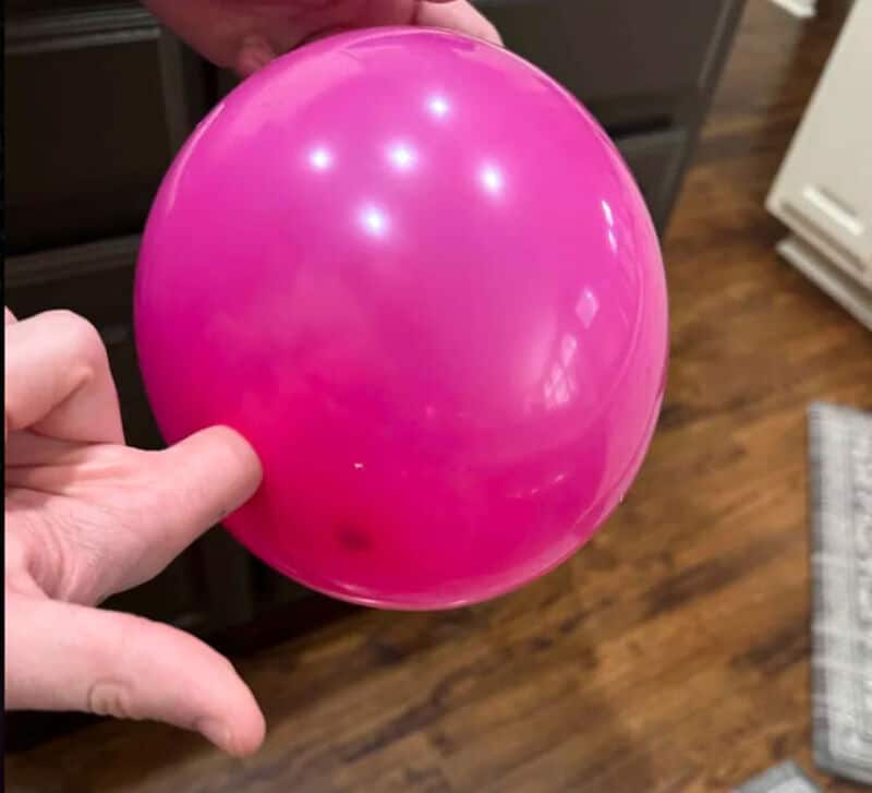 Pink balloon held by hand in a kitchen setting.