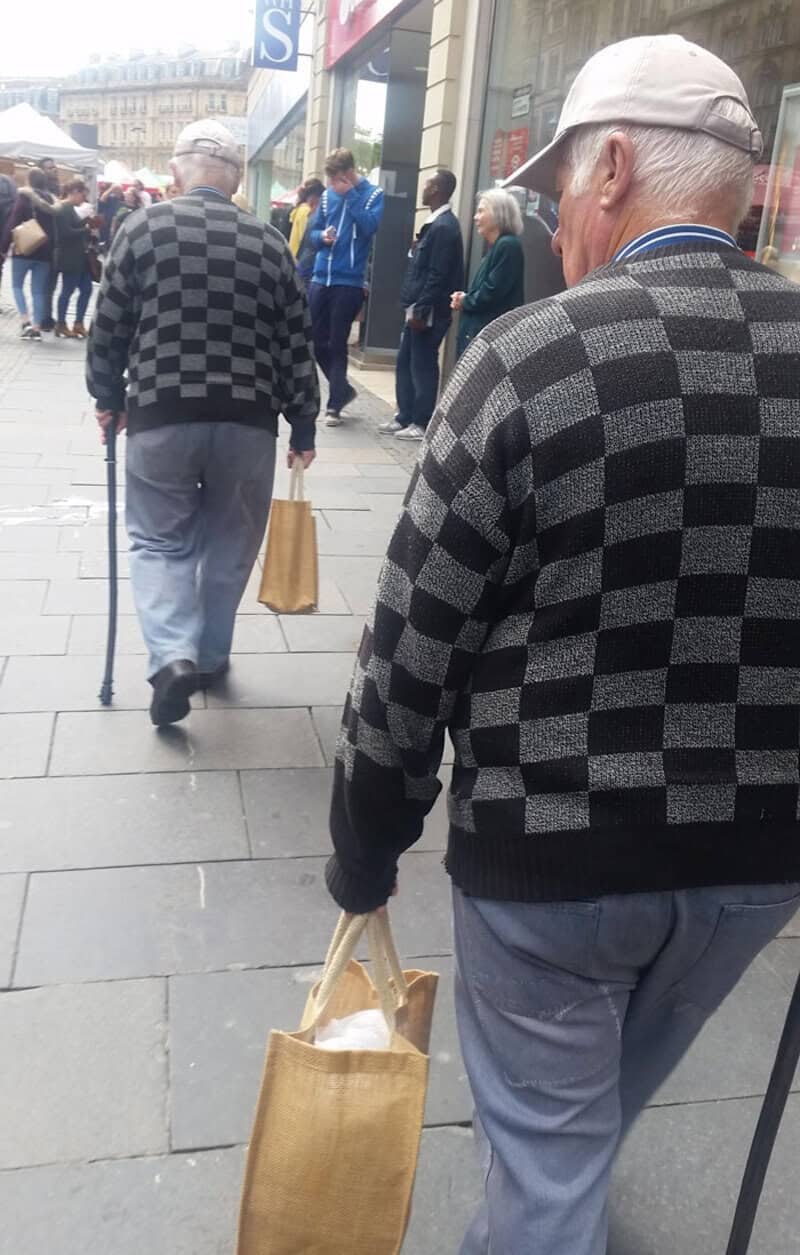 Older man with gray hair in checkered sweater walking on busy street.