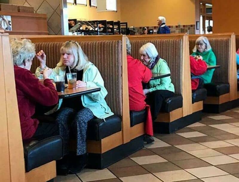 Four elderly women sitting in a booth at a restaurant, two of them talking and two reading.