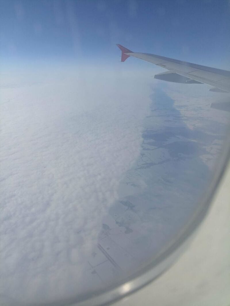 View from airplane window showing wing and clouds below.