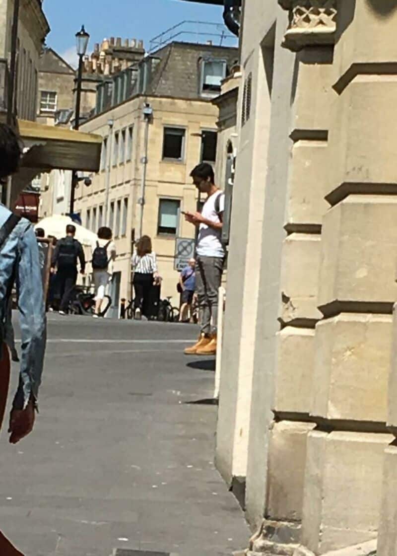 Young man in white shirt and beige pants looking at his phone on a city street.