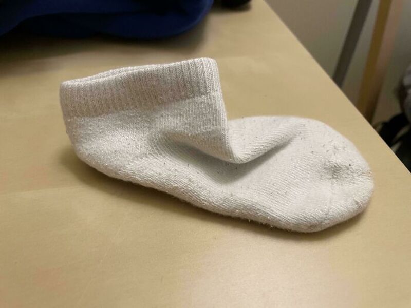 A single white sock lying on a beige surface with a blue object in the background.