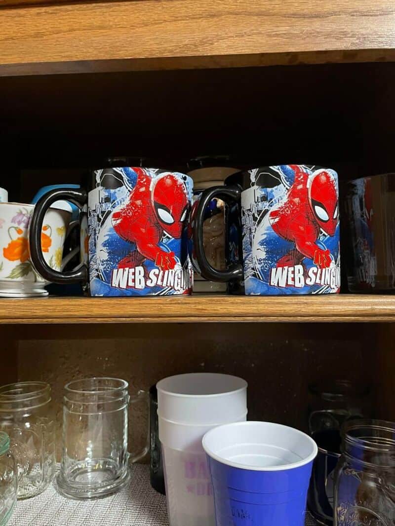 Two Spider-Man mugs with 'Web Slingers' on a wooden shelf.