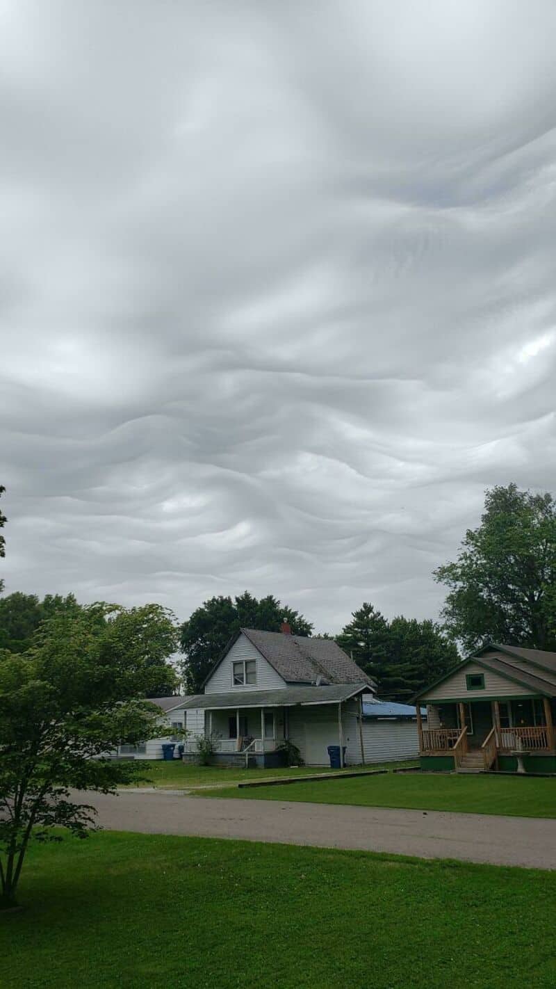 Overcast sky with swirling gray clouds over suburban houses and trees.