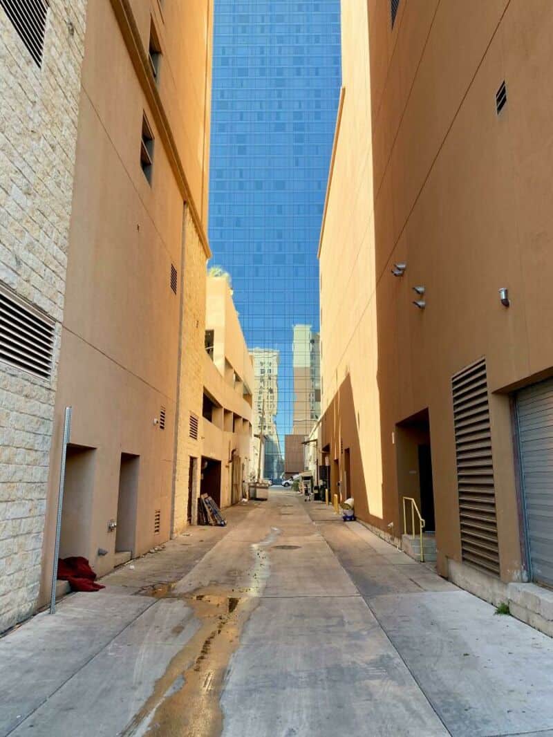 Narrow alley between tall buildings with a blue glass skyscraper in the background.