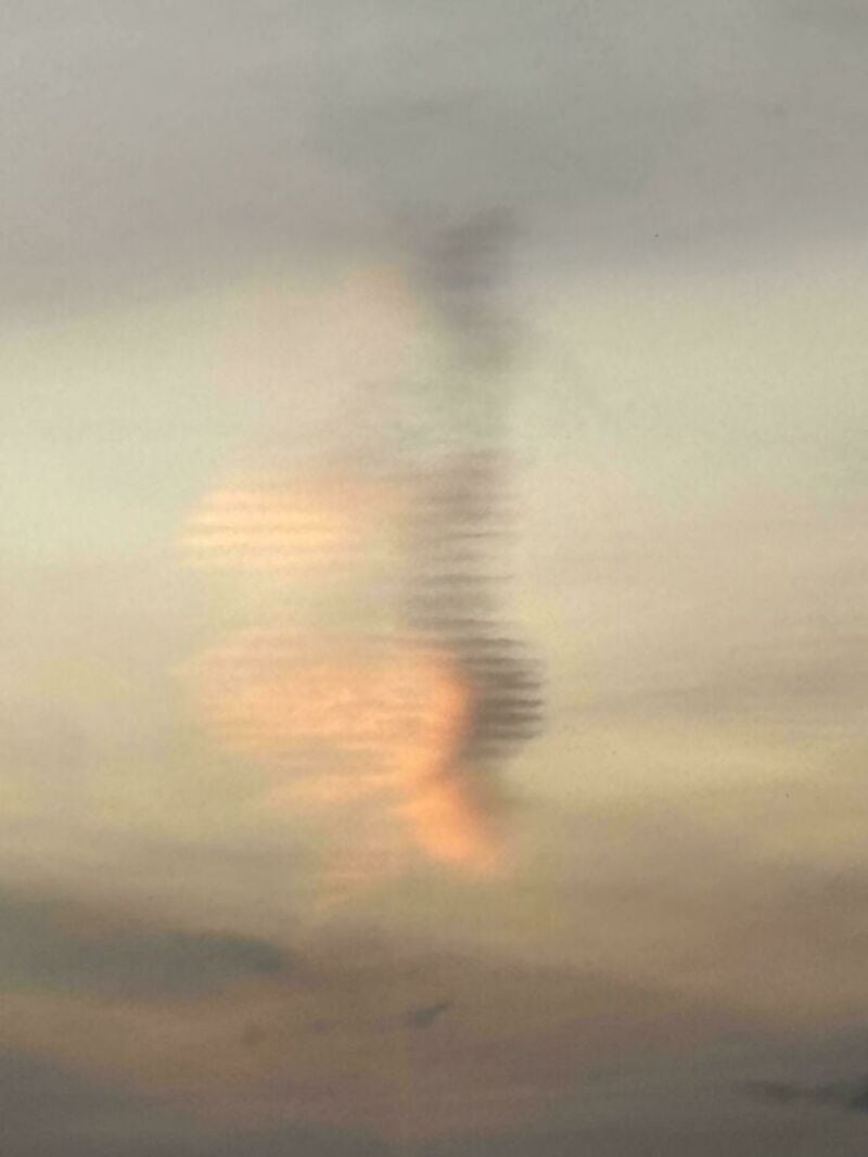 Blurry image of a tornado-like formation over water with a rainbow reflection.
