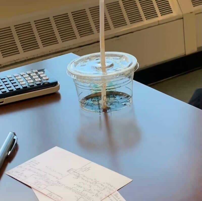Clear plastic cup with a straw on a desk, with a calculator and paper notes nearby.