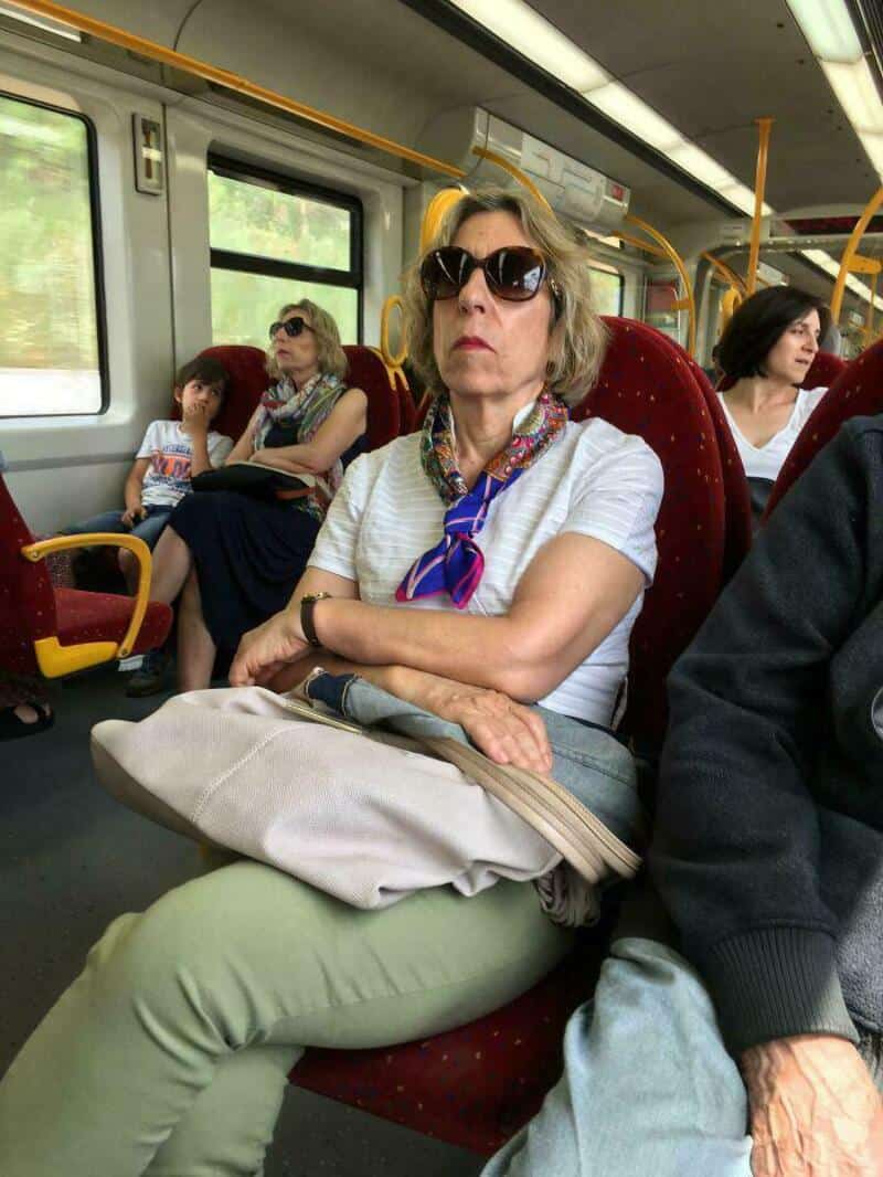 Woman with sunglasses sitting on a train with other passengers.