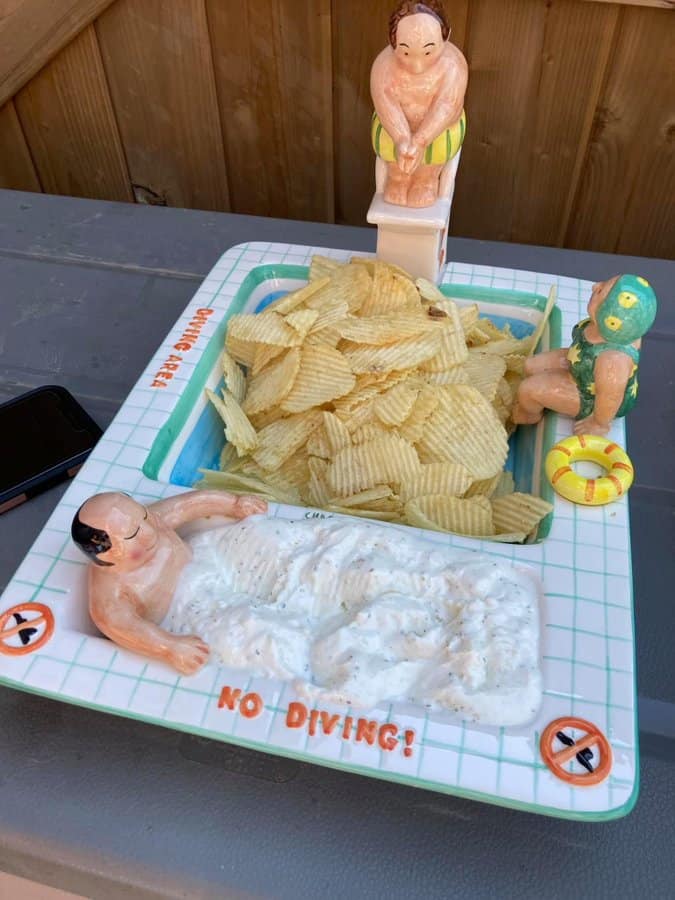 Humorous bath scene with figurines and potato chips on a tray.