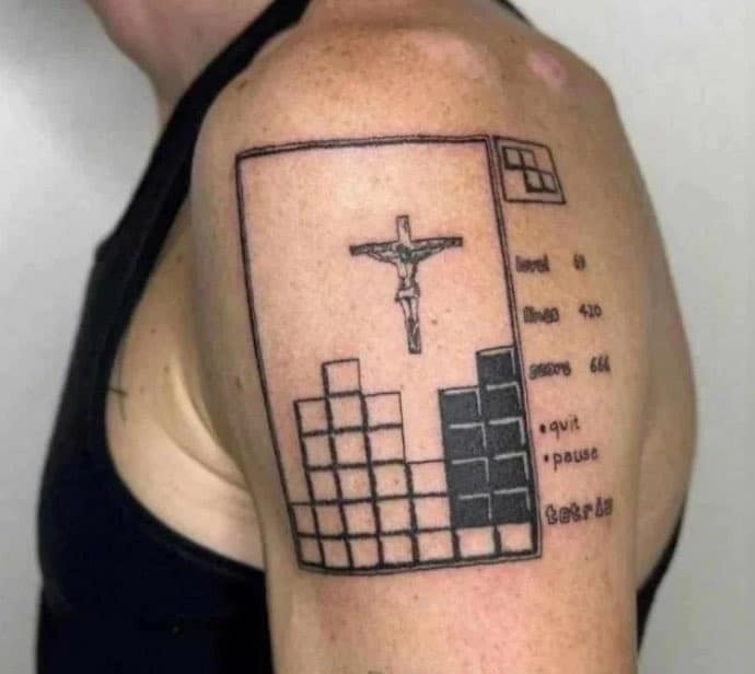 Tattoo of a Tetris game with a crucifix in the center on a person's upper arm.