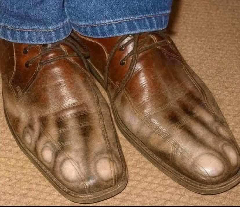 Pair of brown leather shoes with burn marks and creases, worn with jeans.