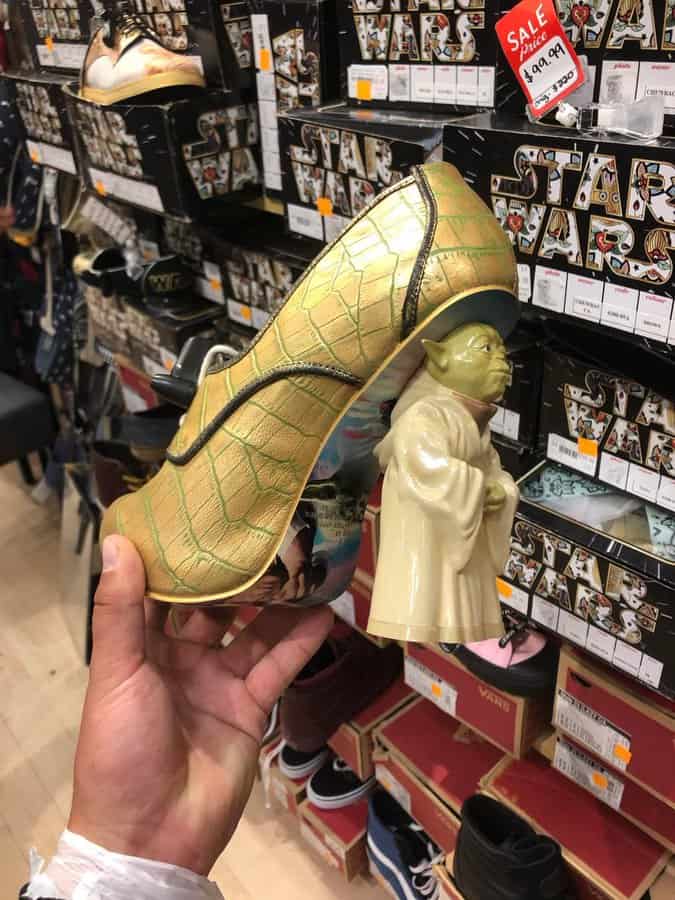 Yoda-shaped shoe with a green and gold design, held in a store aisle.
