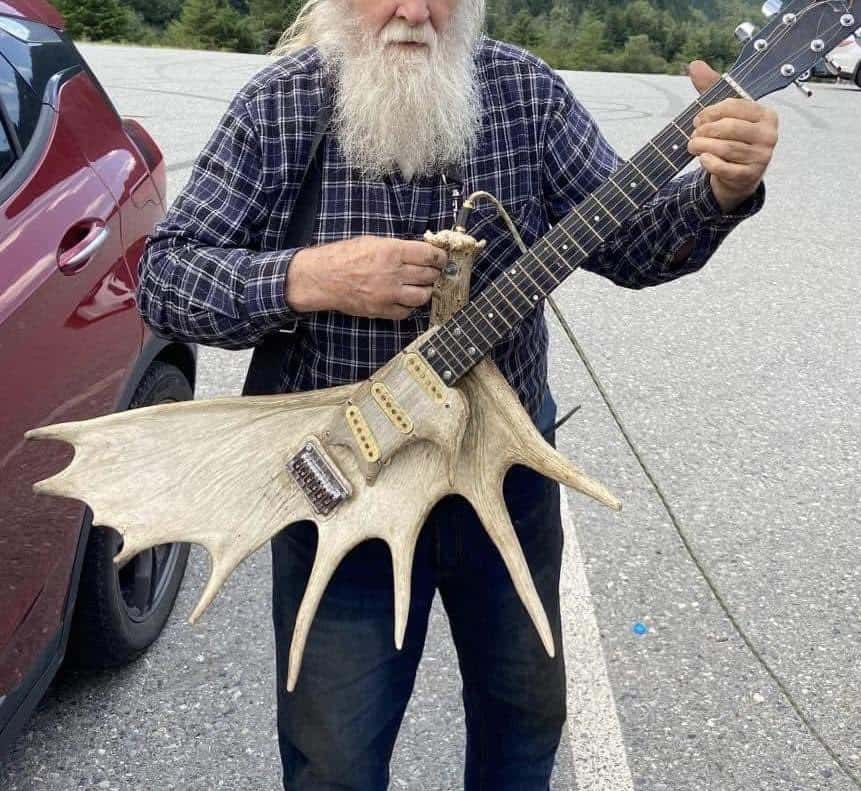 Man with a long white beard holding a guitar with a unique antler-like body.