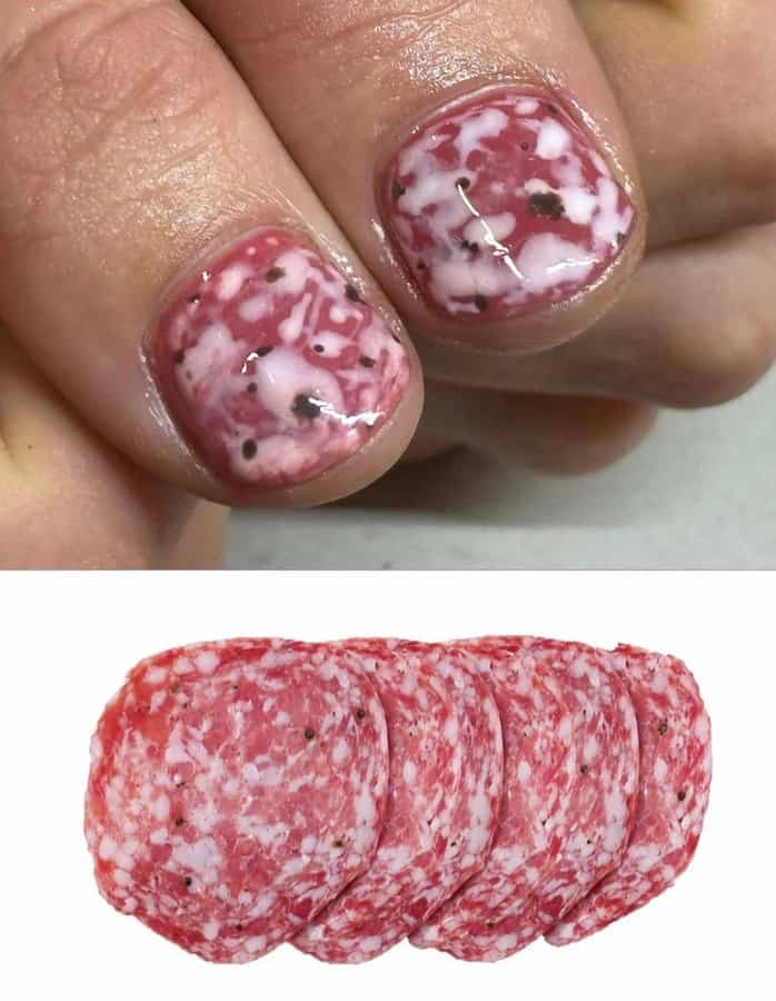 Nail art with pink and white marbled design and black dots, resembling salami slices.